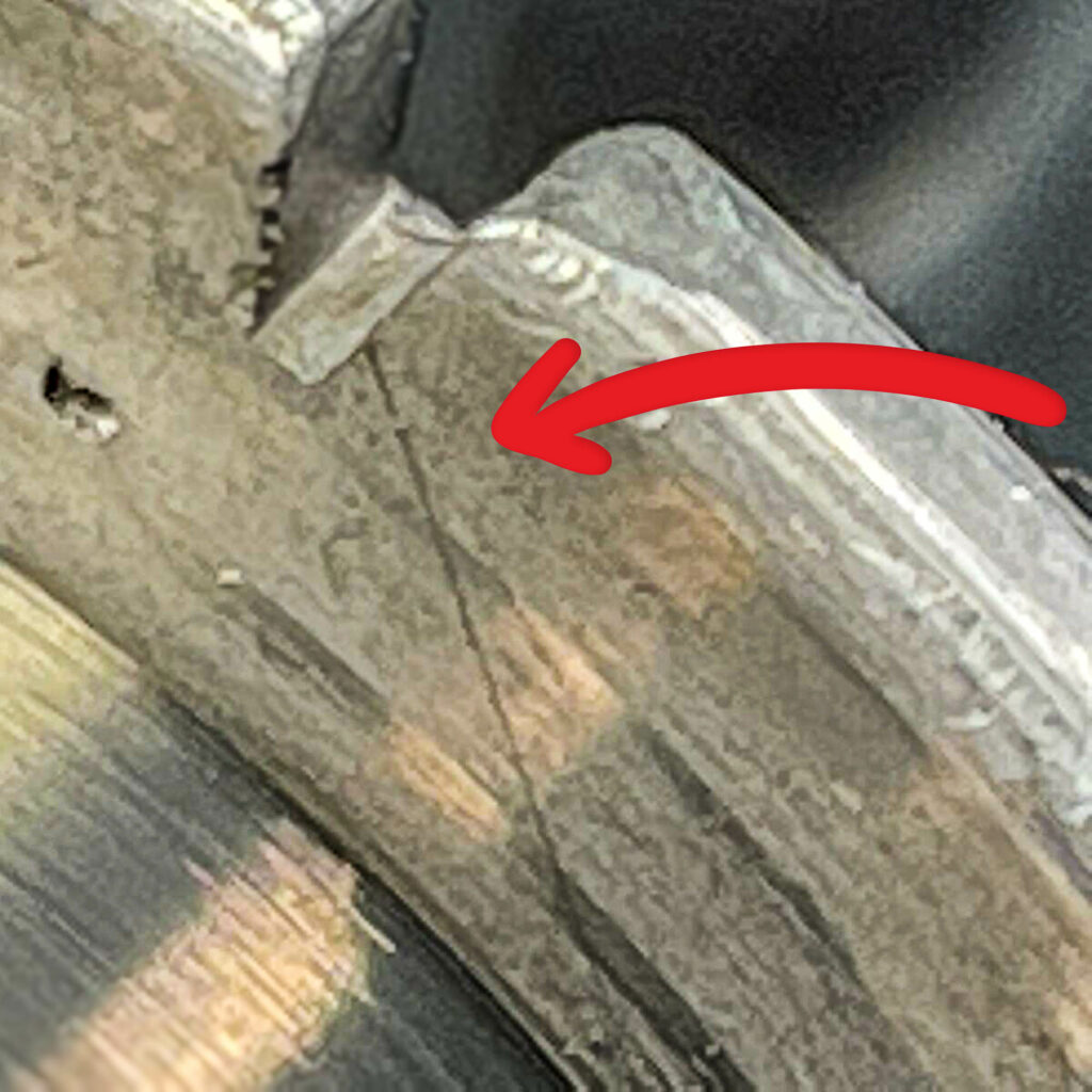 Close-up of a roll of tungsten wire from 1975 for sale from Obtainium Science and Surplus, showing a crack on the spool's metal rim. A red arrow points to the crack, emphasizing the damage. The surface of the spool appears worn and aged.