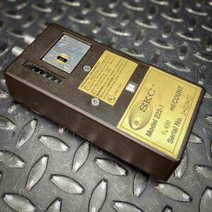 Another angled view of the SKC low-flow personal air sampler model 222 from Obtainium Science and Surplus, displaying the yellow label, counter window, and adjustment dial. The dark brown casing contrasts with the textured metal surface beneath it.